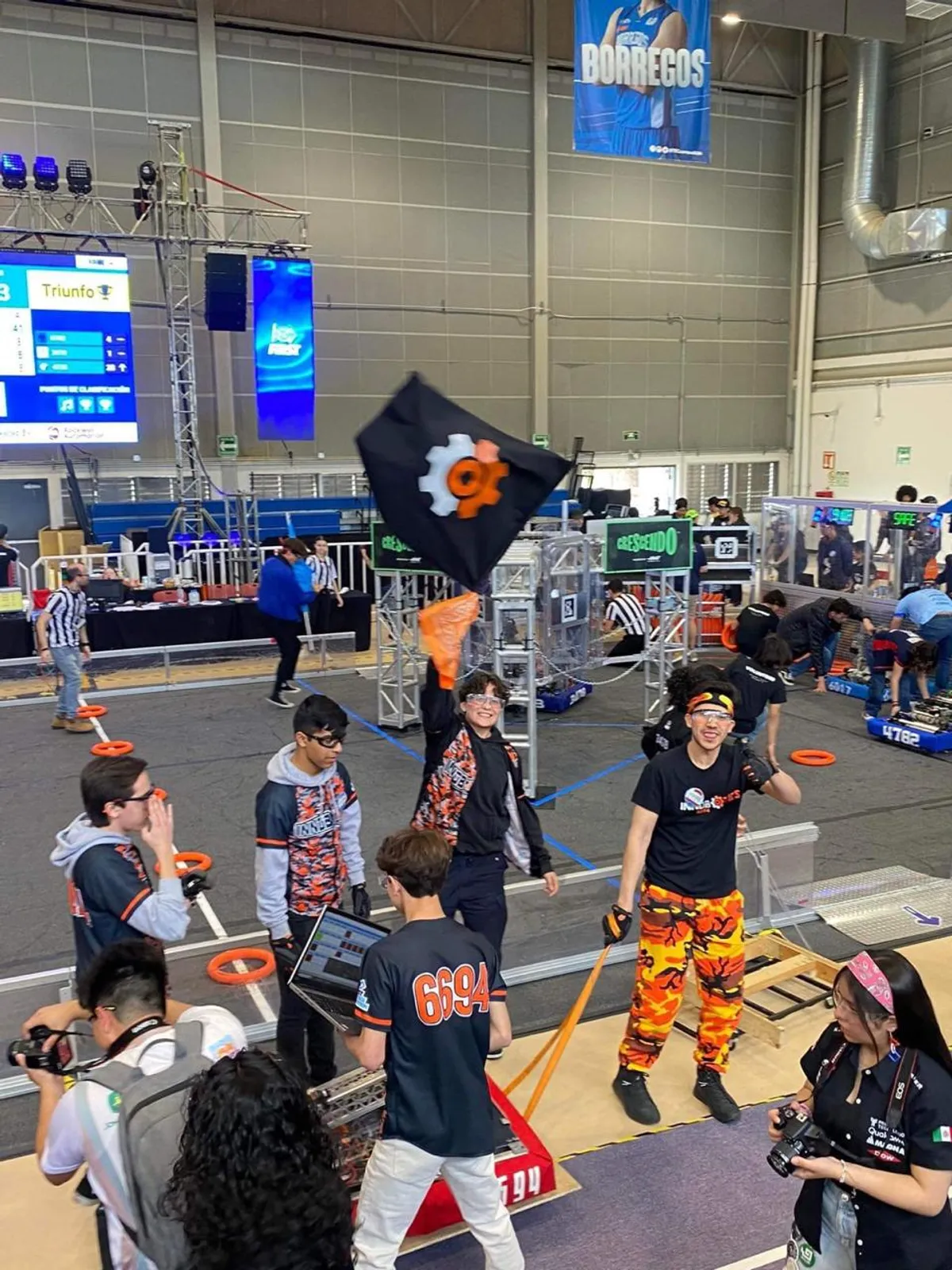 Innobotics team celebrating on the field with the team flag while a teammate reviews code on a laptop