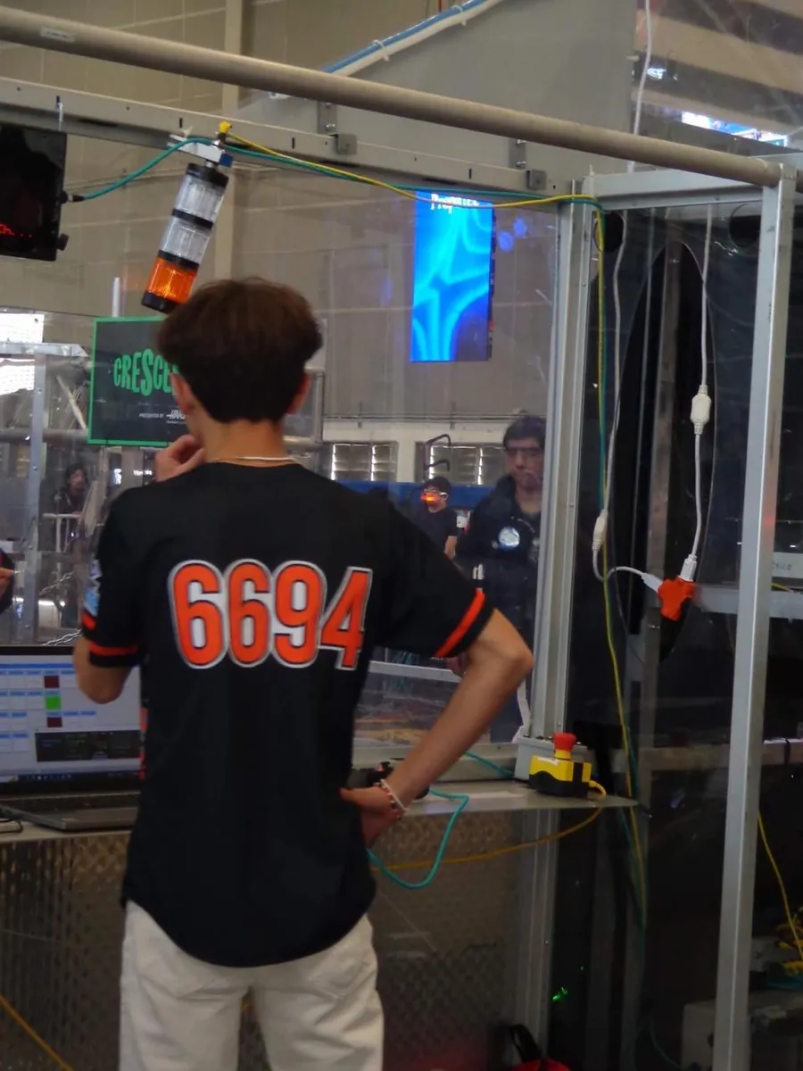 Drive team member in a 6694 jersey at the alliance station glass with match telemetry on a laptop